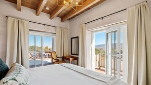A bedroom with a large bed, a desk, and a chair, with a balcony and a view of the outdoors. - Santa Fe Santuario- Perfect Views, Kiva Fireplace (Santa Fe)