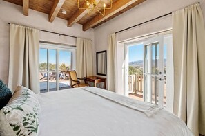 Une chambre dotée d’un grand lit, d’un bureau et d’une chaise, avec un balcon et une vue sur l’extérieur.