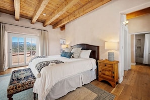 A bedroom with a large bed, a wooden nightstand, a patterned rug, and a view through a glass door. - Santa Fe Santuario- Perfect Views, Kiva Fireplace (Santa Fe)