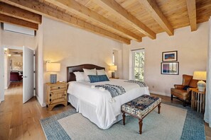 A bedroom with a wooden ceiling, a large bed with multiple pillows, bedside tables with lamps, a chair, and a window with a view. - Santa Fe Santuario- Perfect Views, Kiva Fireplace (Santa Fe)