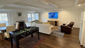 Een moderne woonkamer met een tafelvoetbaltafel, een open haard, een televisie en een bruine leren bank.