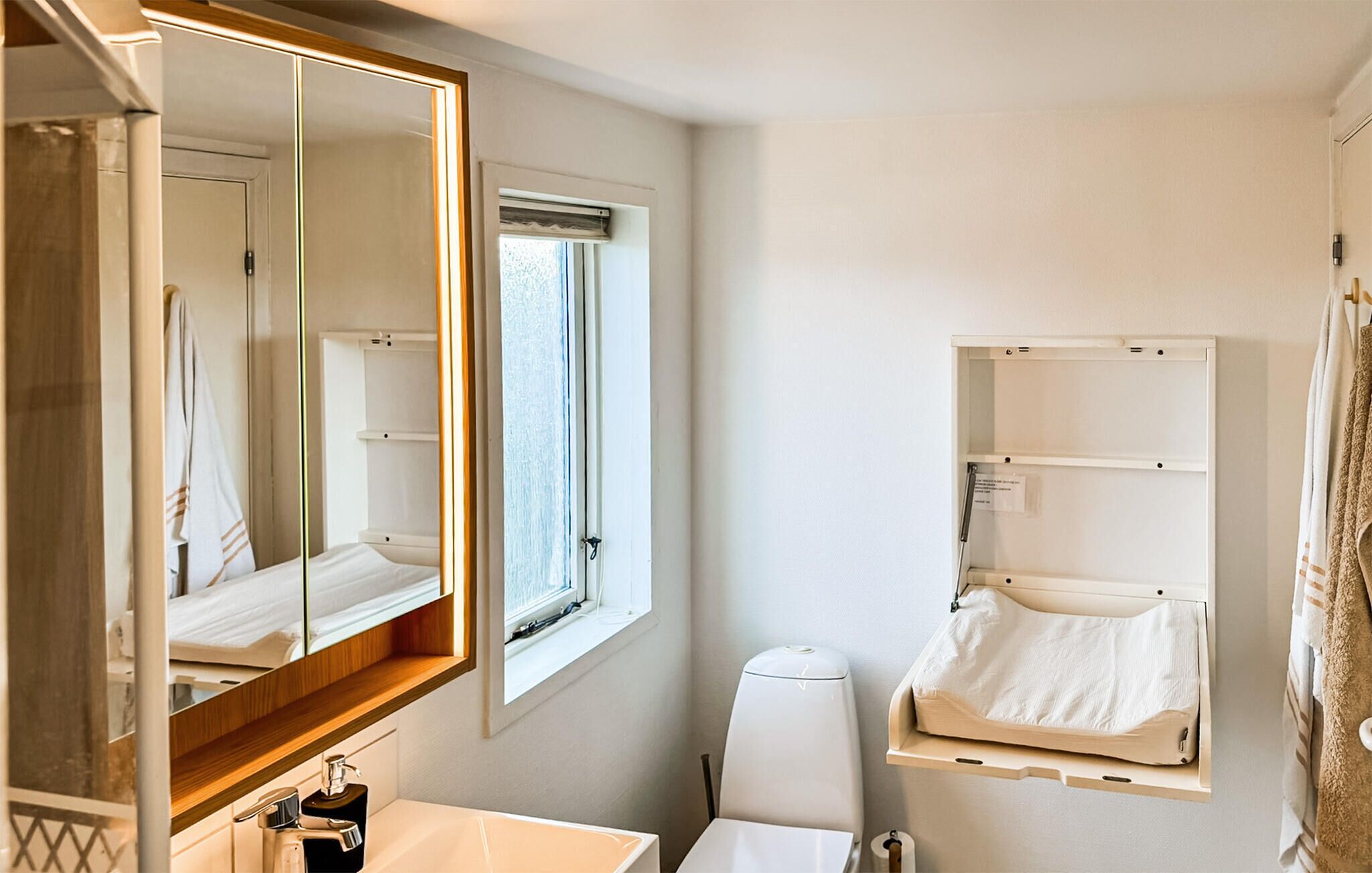 Une salle de bain avec un grand miroir, un lavabo, des toilettes et une fenêtre.
