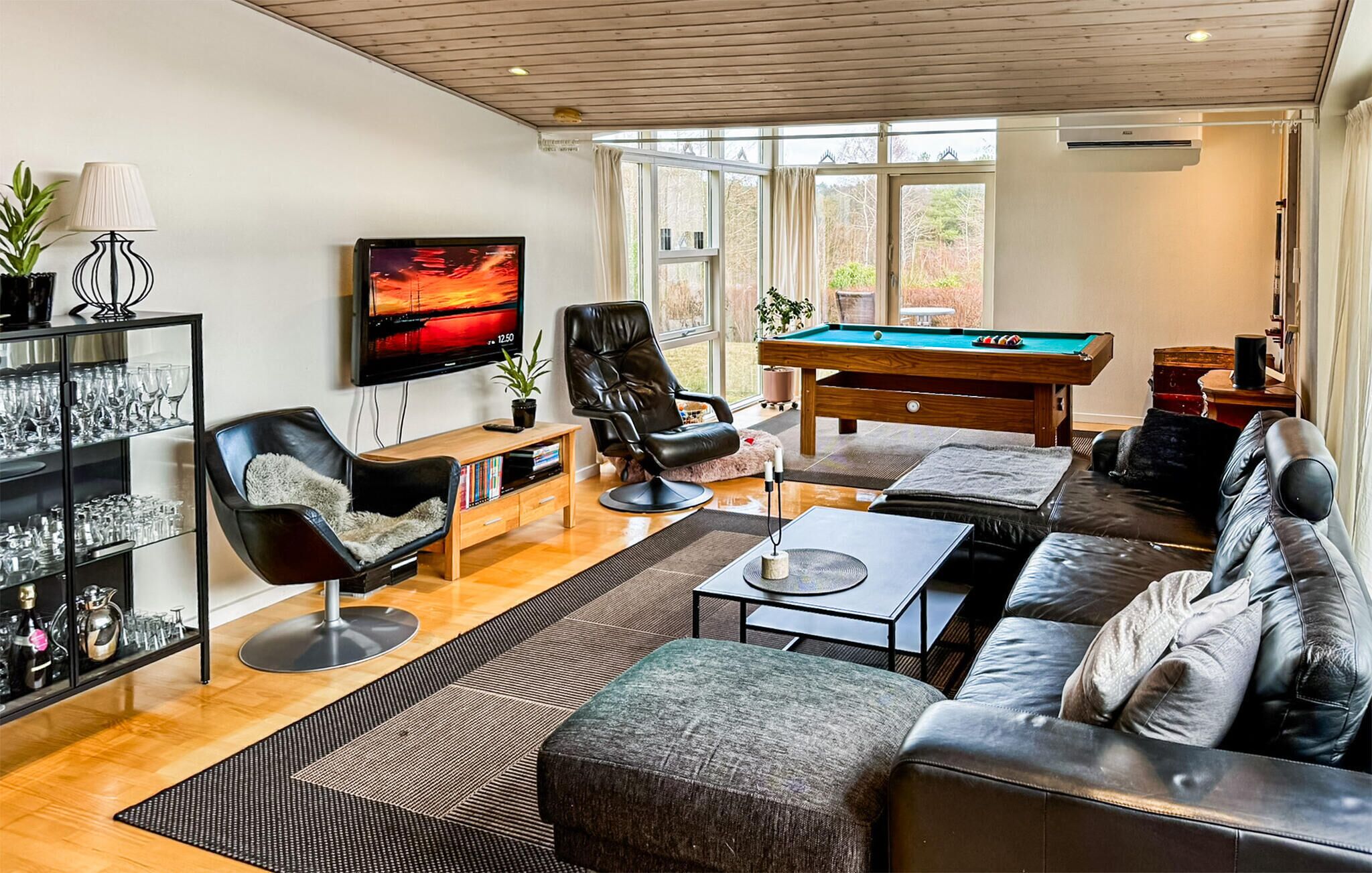 Een moderne woonkamer met een pooltafel, leren banken, een televisie en een glazen kast.