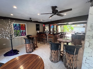 A bar area with wooden furniture, ceiling fans, and artwork on the walls. - Walk to Waterfront! Luxury King Suite w/ Rooftop Pool & Spa (Cozumel)