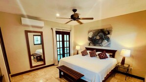 A bedroom with a large bed, a ceiling fan, a bench, a desk, and a large window. - Walk to Waterfront! Luxury King Suite w/ Rooftop Pool & Spa (Cozumel)