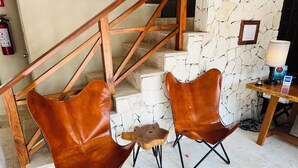 A staircase with wooden railings and a stone wall. There are two brown leather chairs and a small wooden table. A lamp is on a wooden table next to the chairs. - Walk to Waterfront! Luxury King Suite w/ Rooftop Pool & Spa (Cozumel)