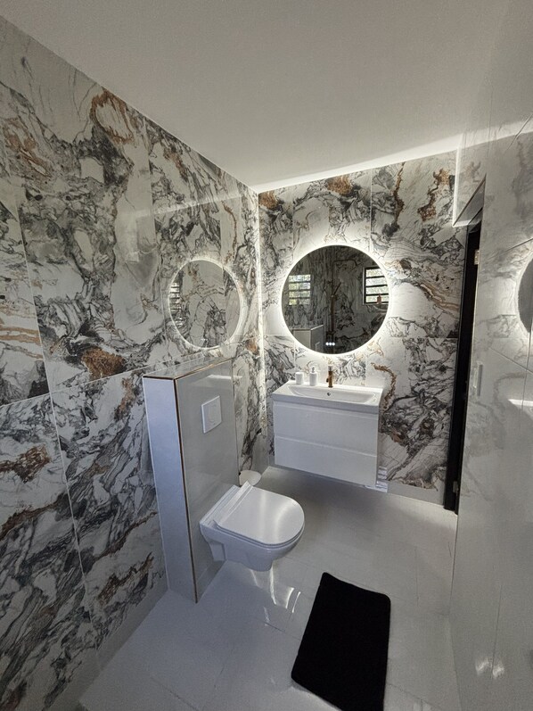 A bathroom with marble walls, a toilet, a sink, and two circular mirrors. - Lux Apartment Stay (Willemstad)