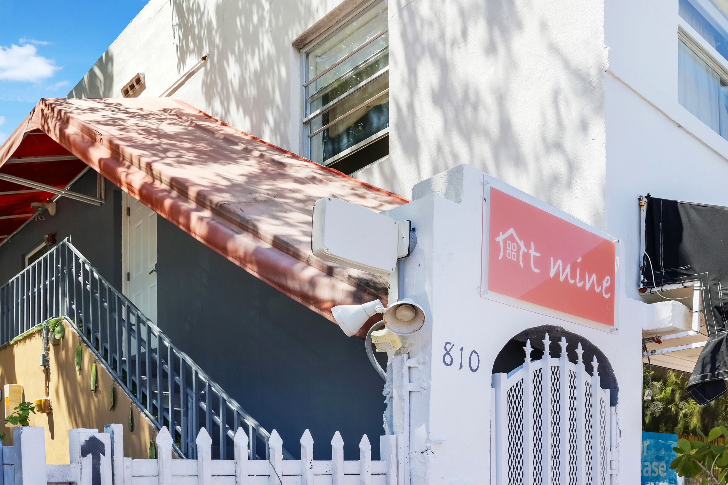Un edificio con fachada blanca, toldo rojo y valla de piquetes blancos.