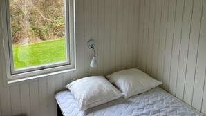 Habitació petita amb un llit individual i finestra que dona a una zona verda.