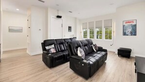 Ein modernes Wohnzimmer mit zwei schwarzen Ledersofas, einem schwarzen Hocker und einem großen Fenster mit Jalousien.