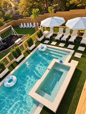 Una piscina con hidromasaje, sillas de descanso y sombrillas.