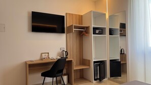 Een moderne hotelkamer met een houten bureau, een zwarte stoel, een flatscreen televisie, een inbouwkleerkast en een kleine koelkast.