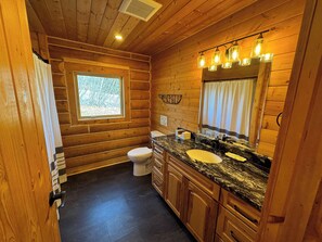 A wooden cabin bathroom with a window, a toilet, a sink, and a mirror.