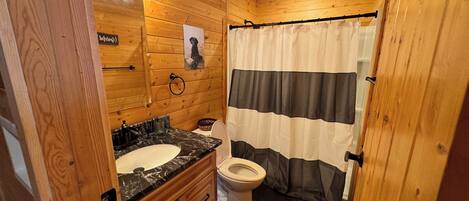 Ein Badezimmer einer Holzhütte mit einem Holzwaschtisch, einer Toilette und einer Duschvorhang.