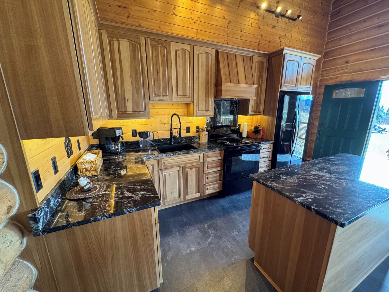 Una cocina moderna con armarios de madera, encimeras de granito y un refrigerador negro.