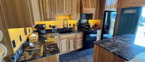 Una cocina moderna con armarios de madera, encimeras de granito y un refrigerador negro.