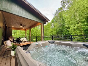A hot tub on a wooden deck with a view of a forest. - 5BR Luxury Cabin w/ Indoor Pool, Theater & Hot Tub (Sevierville)