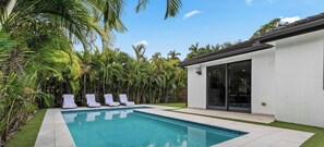 Ein Swimmingpool mit vier Liegestühlen, umgeben von üppiger tropischer Vegetation.