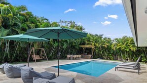 Ein Swimmingpool mit Liegestühlen, einer Schaukel und einem Pergola mit Tisch und Stühlen.