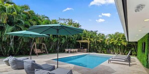 A swimming pool with lounge chairs, a swing set, and a pergola with a table and chairs. - Villa Indigo | Heated Pool • Pickleball (Miami)