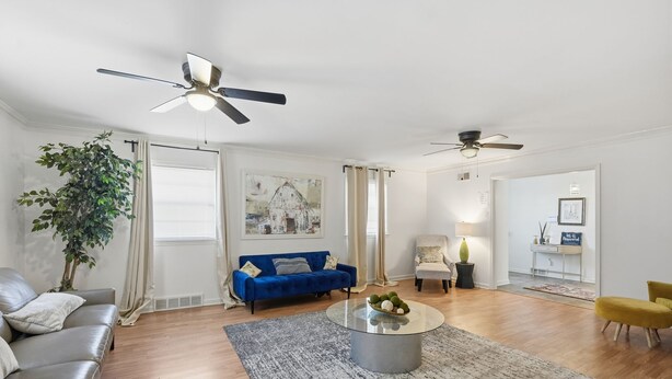 Ein modernes Wohnzimmer mit einem blauen Sofa, einem grauen Sofa, einem gelben Sessel, einem runden Couchtisch und einem Deckenventilator.