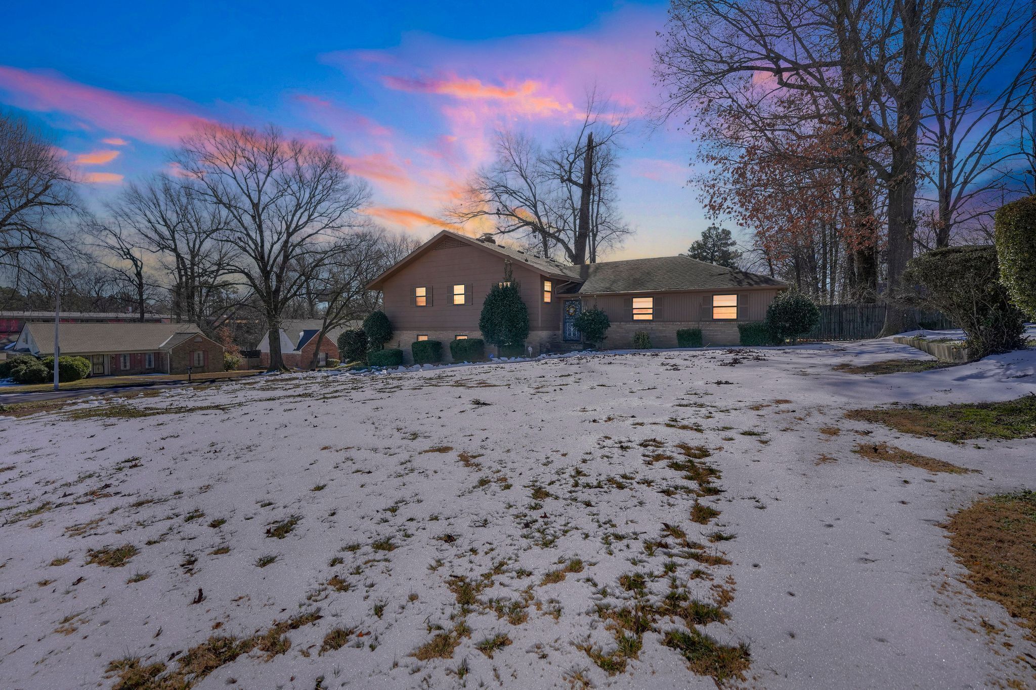 A residential area with two houses, a snow-covered yard, and leafless trees.