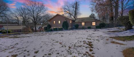 A residential area with two houses, a snow-covered yard, and leafless trees.