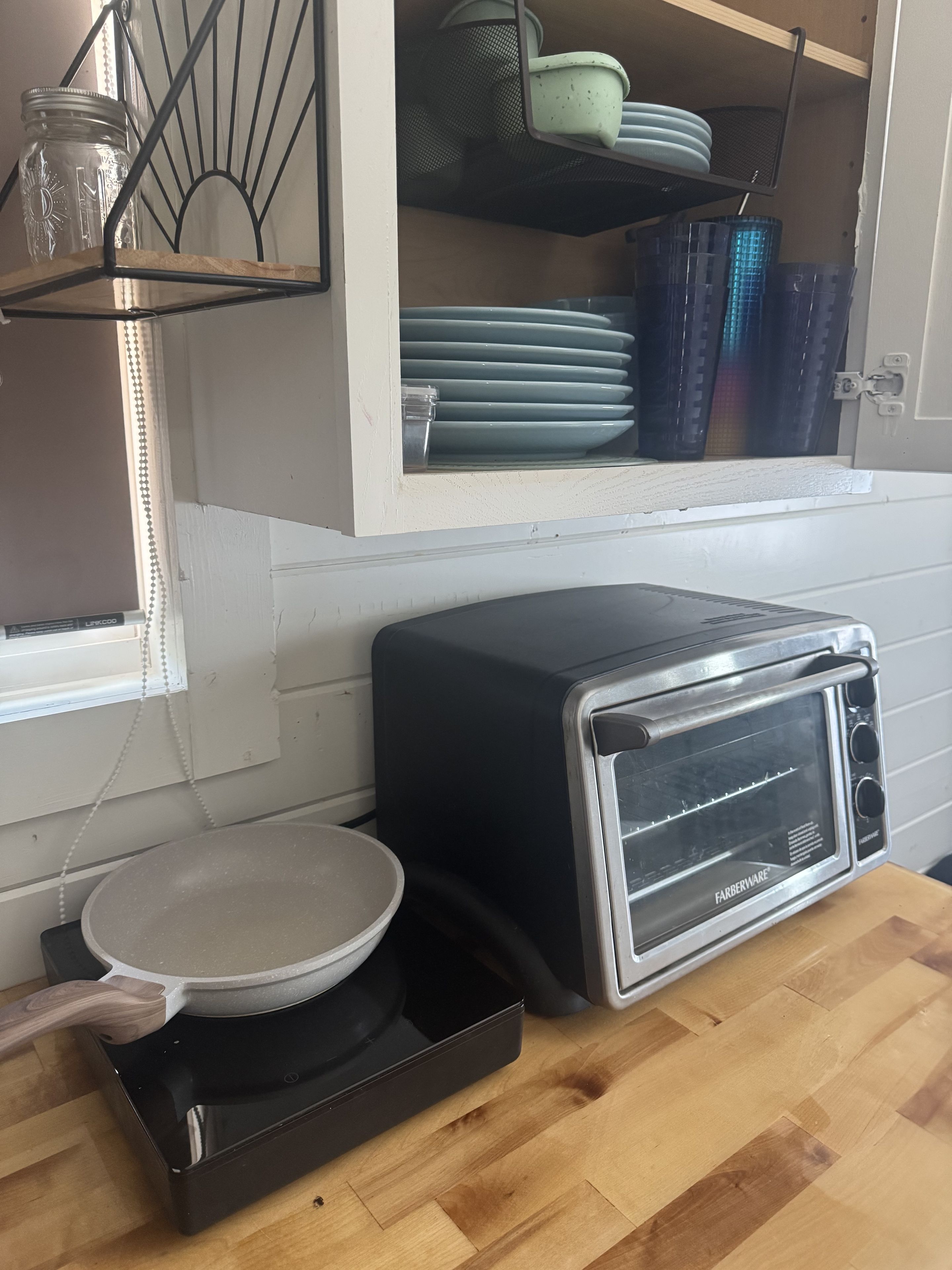 A kitchen with a Farberware toaster oven, a wooden cutting board, and a white bowl.