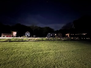 Vista nocturna de una zona rural con una casa pequeña, un granero y un campo.