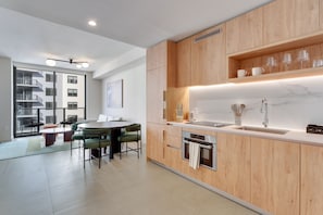 A modern kitchen with wooden cabinets, a marble countertop, and a dining area with a round table and chairs. - Crosby Miami WTC 1BR/1BA Downtown All New #3212 (Miami)