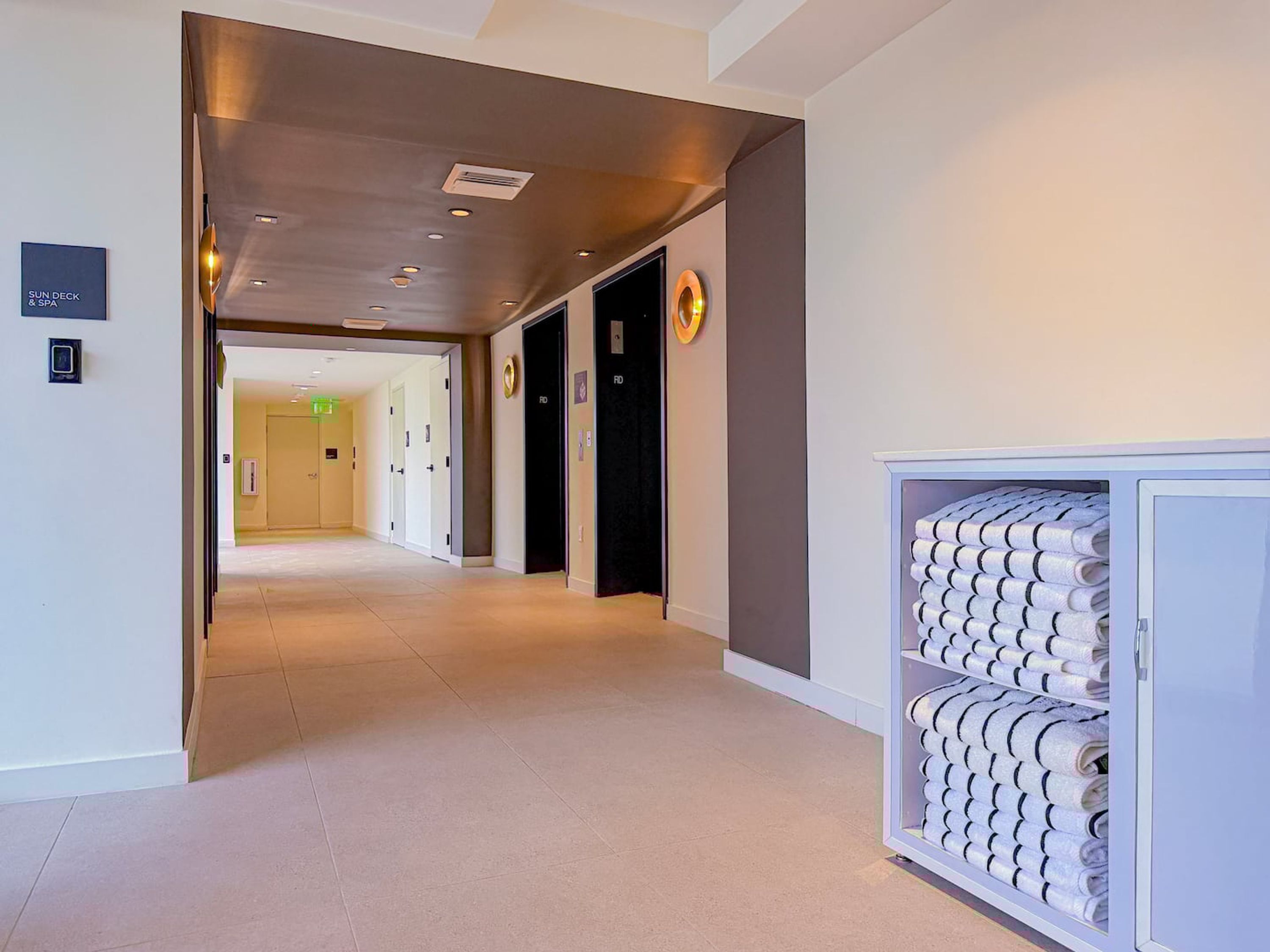 A hotel corridor with a modern design, featuring a reception area, a sun deck sign, and a towel storage unit.