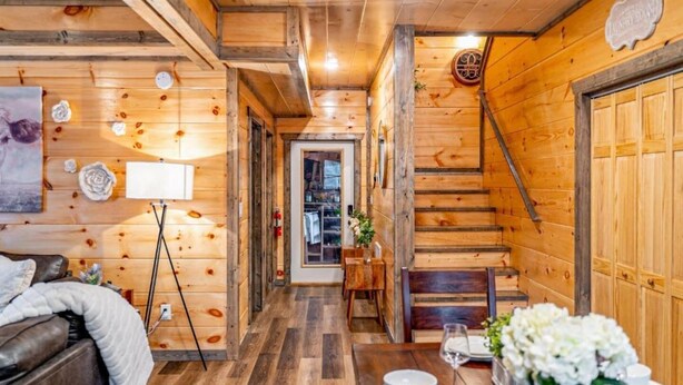 Interior de madera con una escalera, un área de comedor con flores blancas y una cama con una colcha.