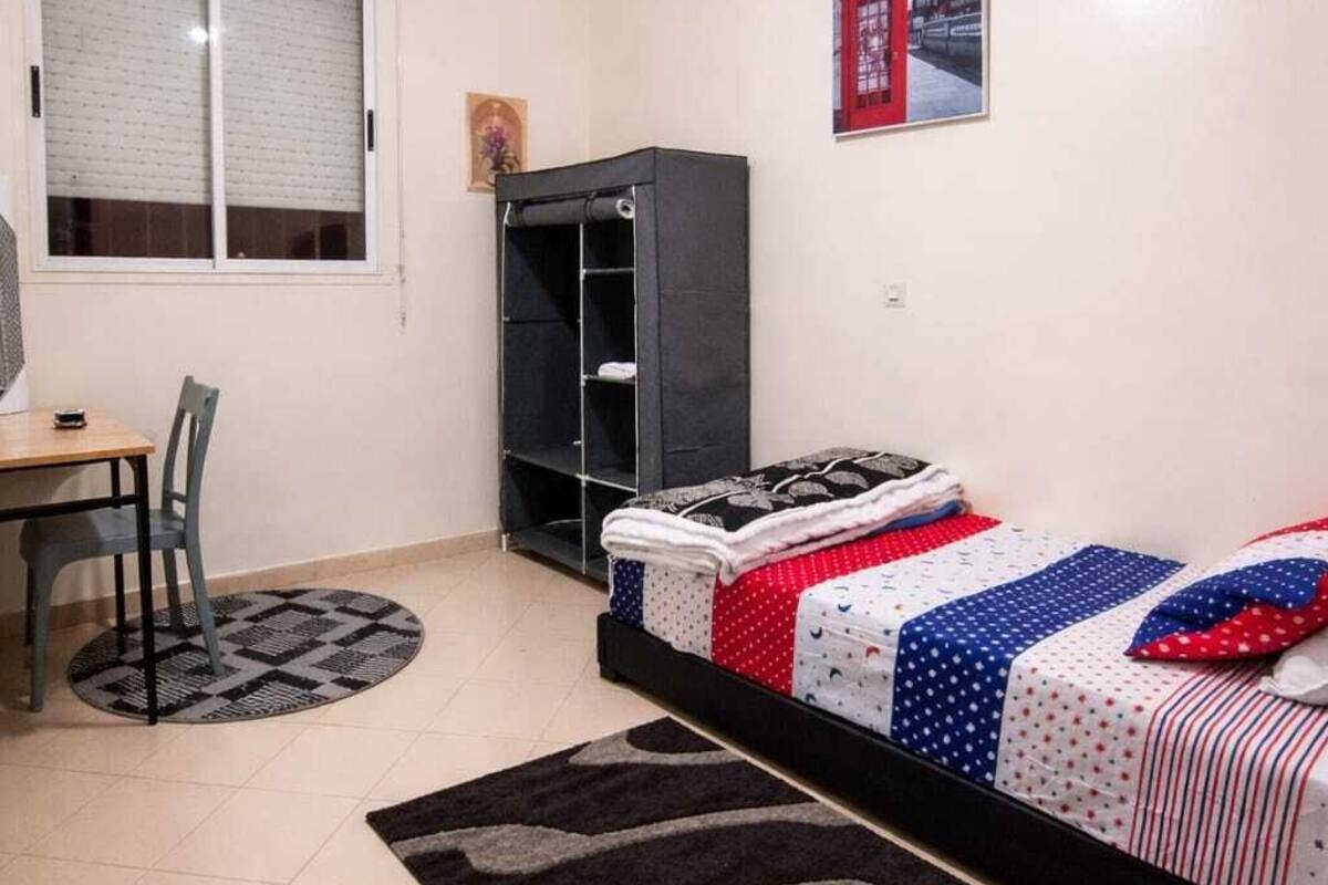A bedroom with a bed, a desk, a chair, a wardrobe, and a window.