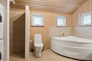 Et moderne badeværelse med træindretning, badekar, toilet og bruseniche.