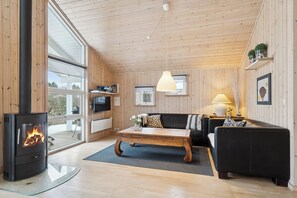 En hyggelig stue med pejs, trævægge, en sofa, et sofabord og et fjernsyn.