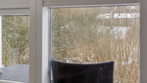 A window with a view of a natural landscape, including trees and a building in the background. - Holiday home with spa and sauna, close to nature (Knebel)
