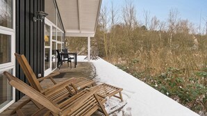 A wooden deck with lounge chairs, a table, and chairs outside a building with large windows. - Holiday home with spa and sauna, close to nature (Knebel)