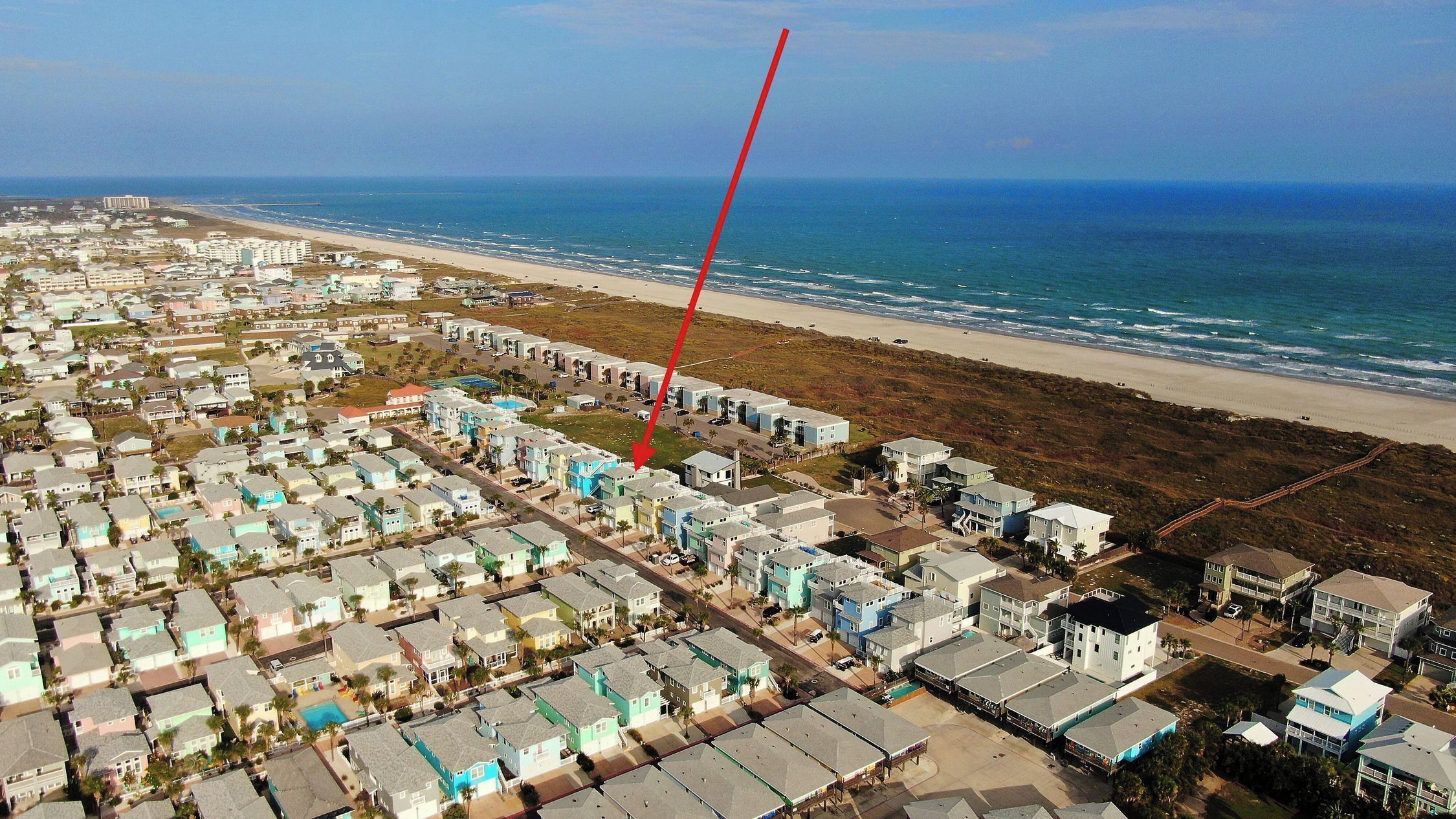 Uma área residencial costeira com propriedades em frente à praia, vista clara do oceano e uma seta vermelha indicando um local específico.