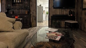 Ein Wohnzimmer mit einer Couch, einem Glastisch mit Zeitschriften, einem Fernseher und einer Holzkommode.