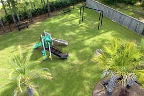 A backyard with a playground, a bench, and palm trees.