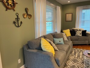 A living room with two grey sofas, a patterned rug, and nautical decor including a ship's wheel and anchor.