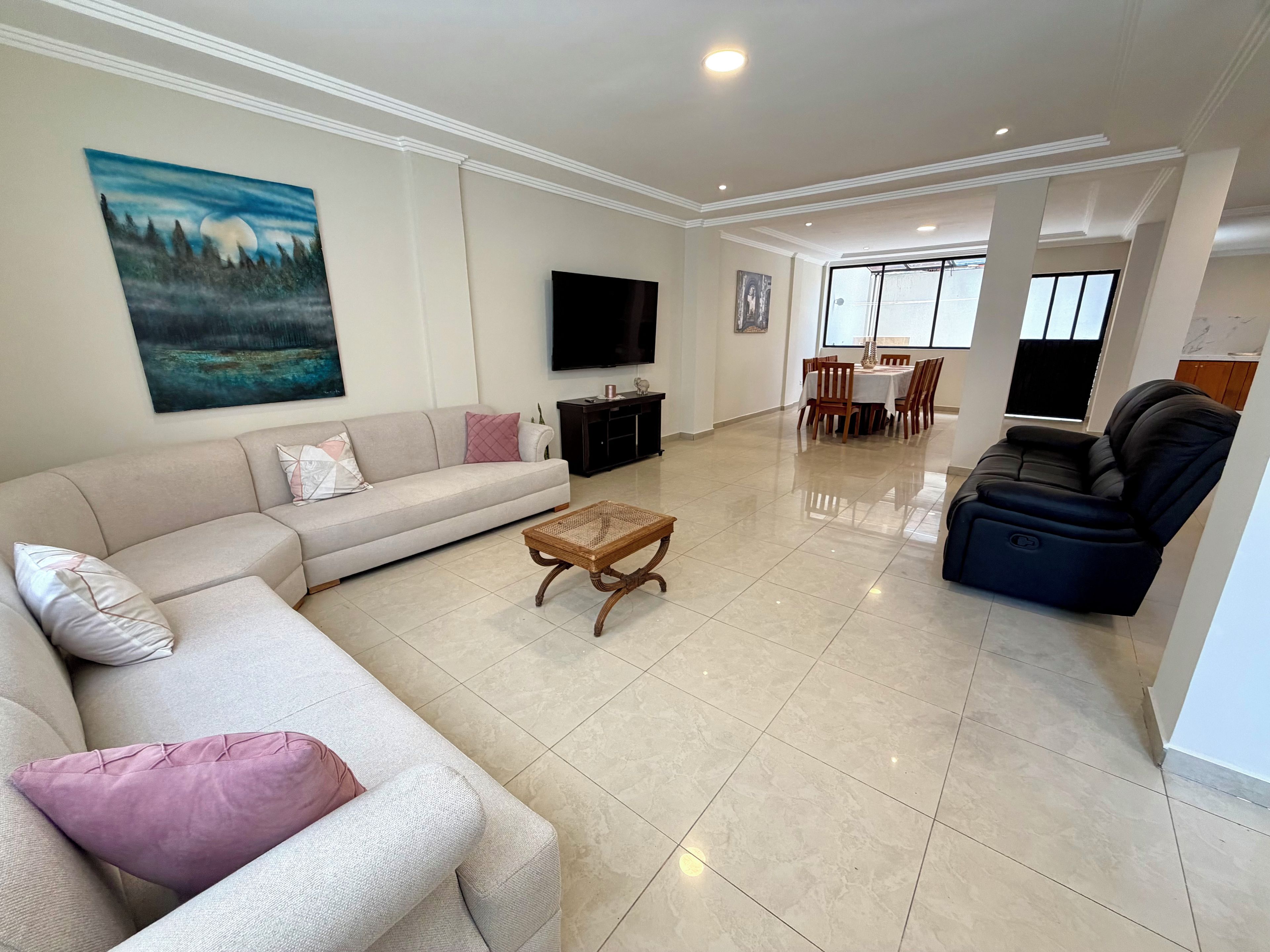Una sala de estar con sofá, mesa de centro, televisor de pantalla plana y comedor con sillas y una mesa.