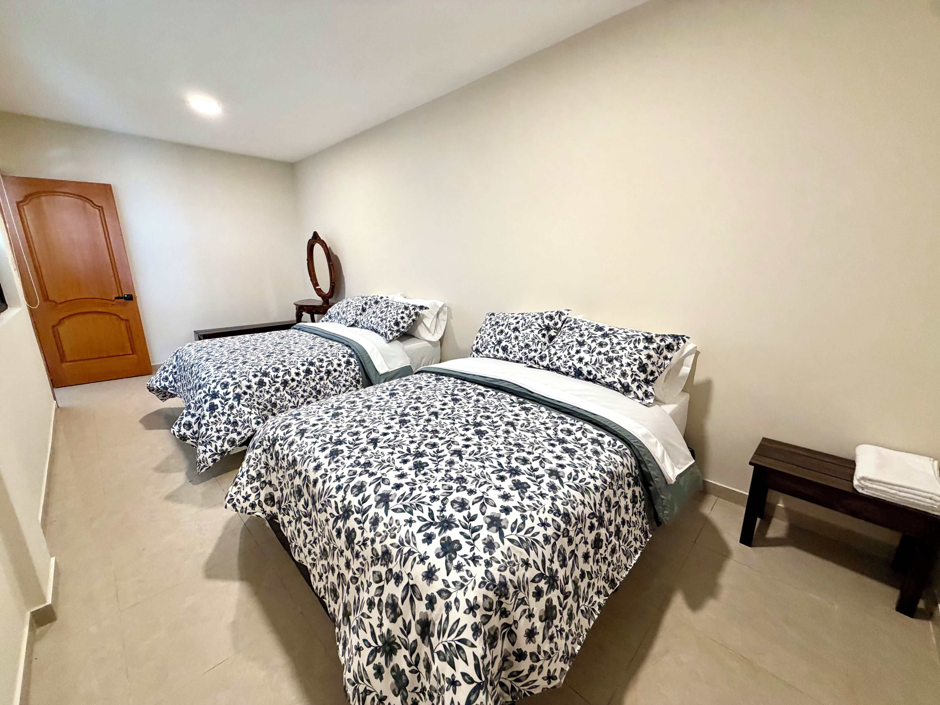 Un dormitorio con dos camas, una puerta de madera, una mesita con una toalla y un espejo en la pared.