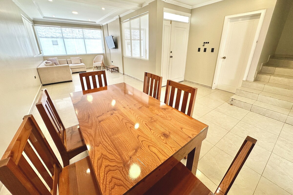Un grand espace de salle à manger avec une table et des chaises en bois, un canapé et un téléviseur en arrière-plan.