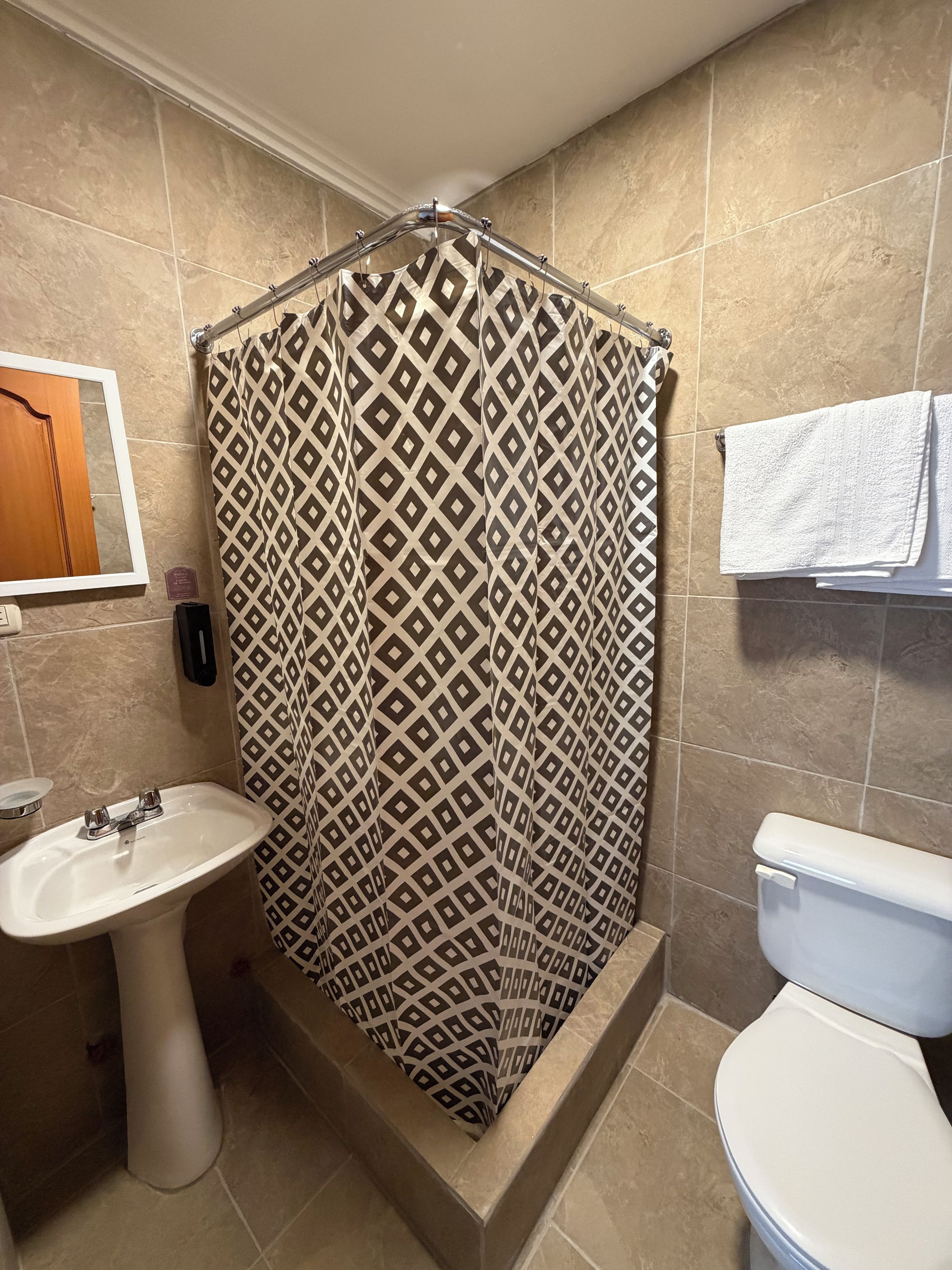 A bathroom with a shower curtain, a sink, a toilet, and a towel rack.