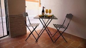 Une petite table avec deux chaises, une bouteille de vin, deux verres et quelques citrons, le tout posé sur un sol carrelé.