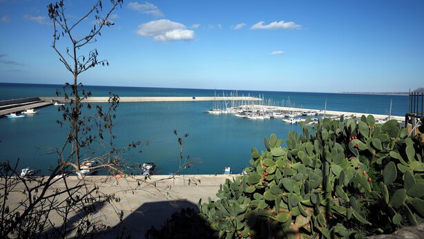 Un port de plaisance sur la côte, avec des bateaux amarrés, une plage de sable et un ciel bleu dégagé.