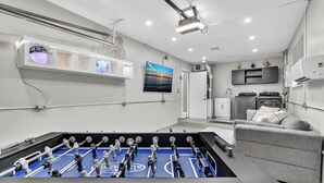 Une pièce moderne avec une table de baby-foot, un canapé gris et un téléviseur fixé au mur.