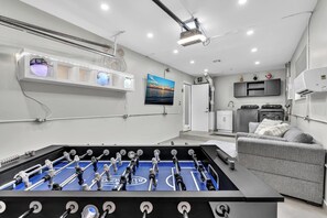 A modern room with a foosball table, a grey sofa, and a TV mounted on the wall. - Beautiful Luxury Waterfront Heated Pool Home in Fort Lauderdale (Fort Lauderdale)