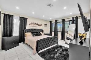 A modern bedroom with a large bed, a vanity with a mirror, and a dresser. - Beautiful Luxury Waterfront Heated Pool Home in Fort Lauderdale (Fort Lauderdale)